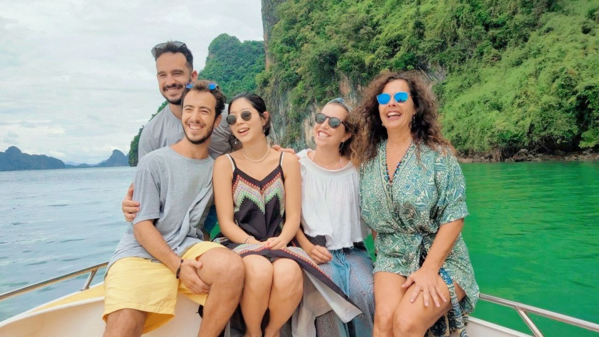 Cinco viajeros sonrientes en la proa de una lancha, frente a un acantilado cubierto de selva y agua verde